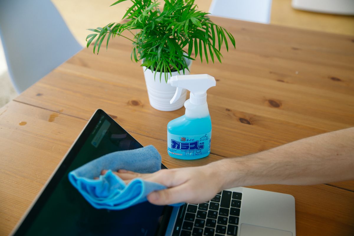 A hand wiping a laptop display with a blue cloth