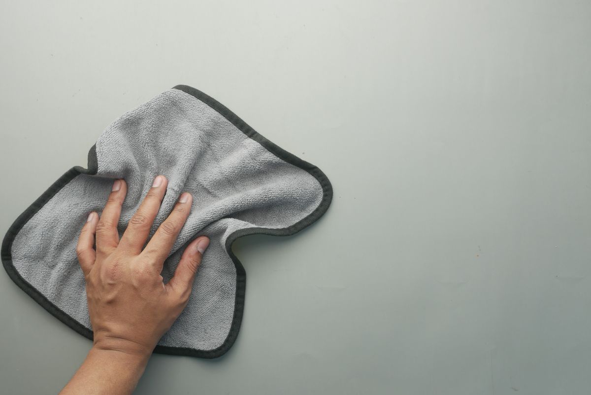 A hand wiping a table with a grey microfibre cloth