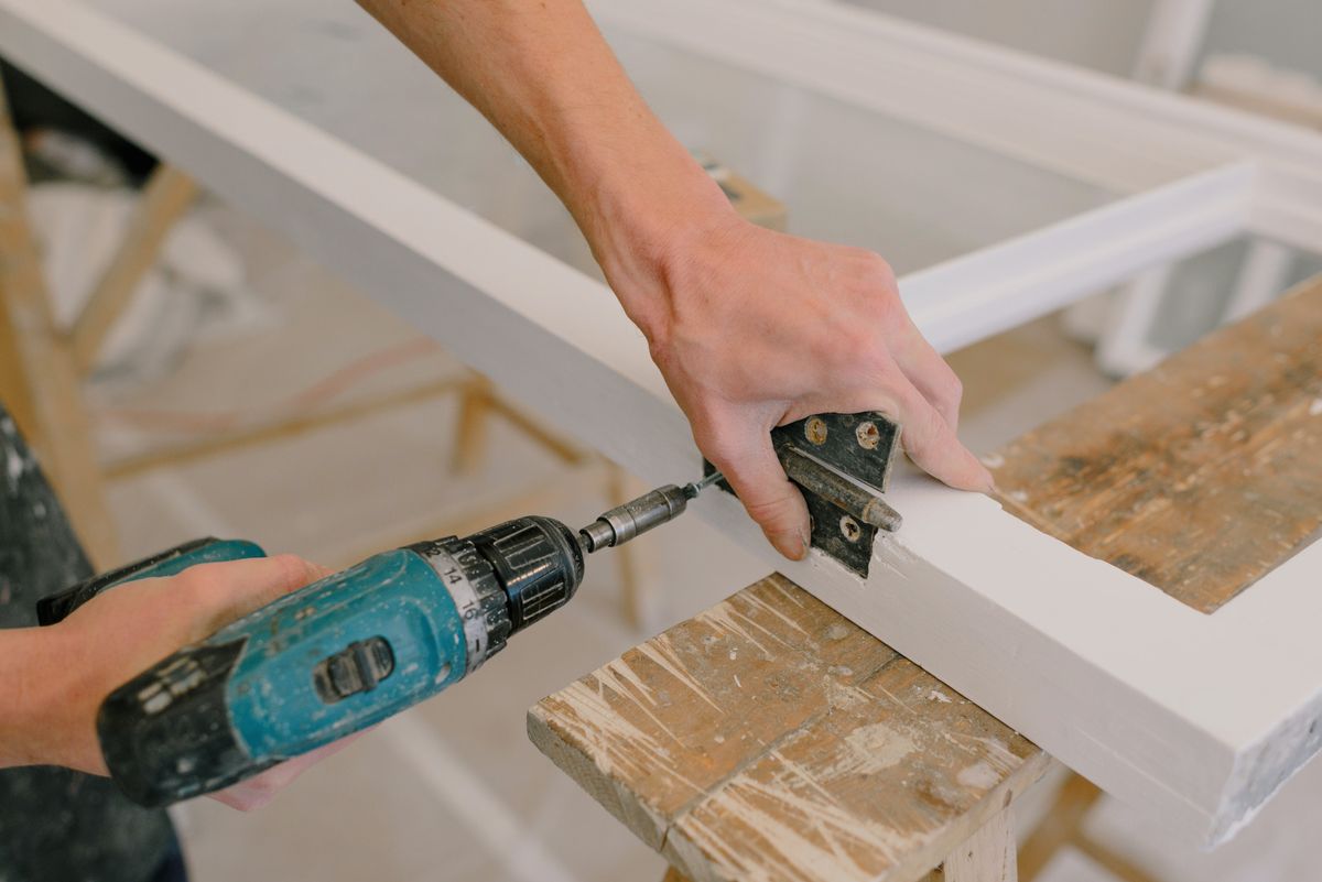 A metal butt hinge being fitted to a white wooden frame with a cordless screwdriver